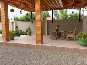An outdoor patio area with wooden furniture, potted plants, and a pergola structure.