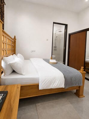 A neatly made bed with white linens, a grey blanket, and a wooden headboard.