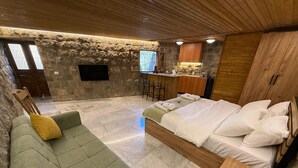 A modern room with a green sofa, a wooden bed, a stone wall, a TV, and a kitchen area.