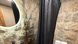 A bathroom with a stone wall, a sink with a mirror, a toilet, and a shower curtain.