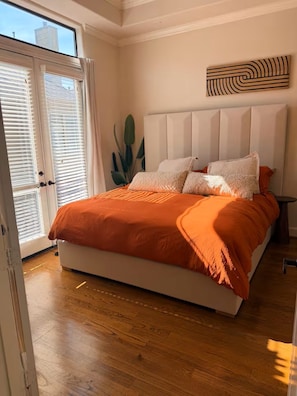 Ein Schlafzimmer mit einem großen Bett, einem Fenster mit Jalousien, einer Pflanze und einem Wandbild.