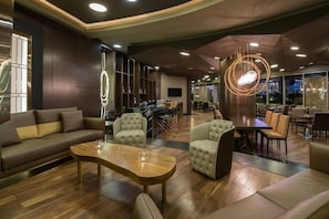 A modern hotel lobby with a sofa, armchairs, a wooden coffee table, and a dining area with chairs and a table. - eko VİLLA (T'bilisi)