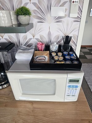 A microwave with a digital control panel, a tray of food items, and a decorative wall with leaf patterns.