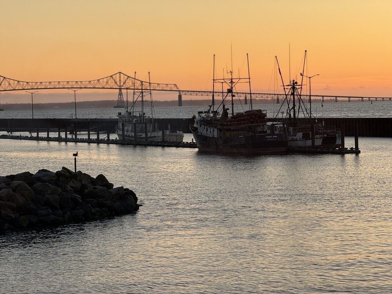A harbor with a large ship docked, a bridge in the background, and calm water.