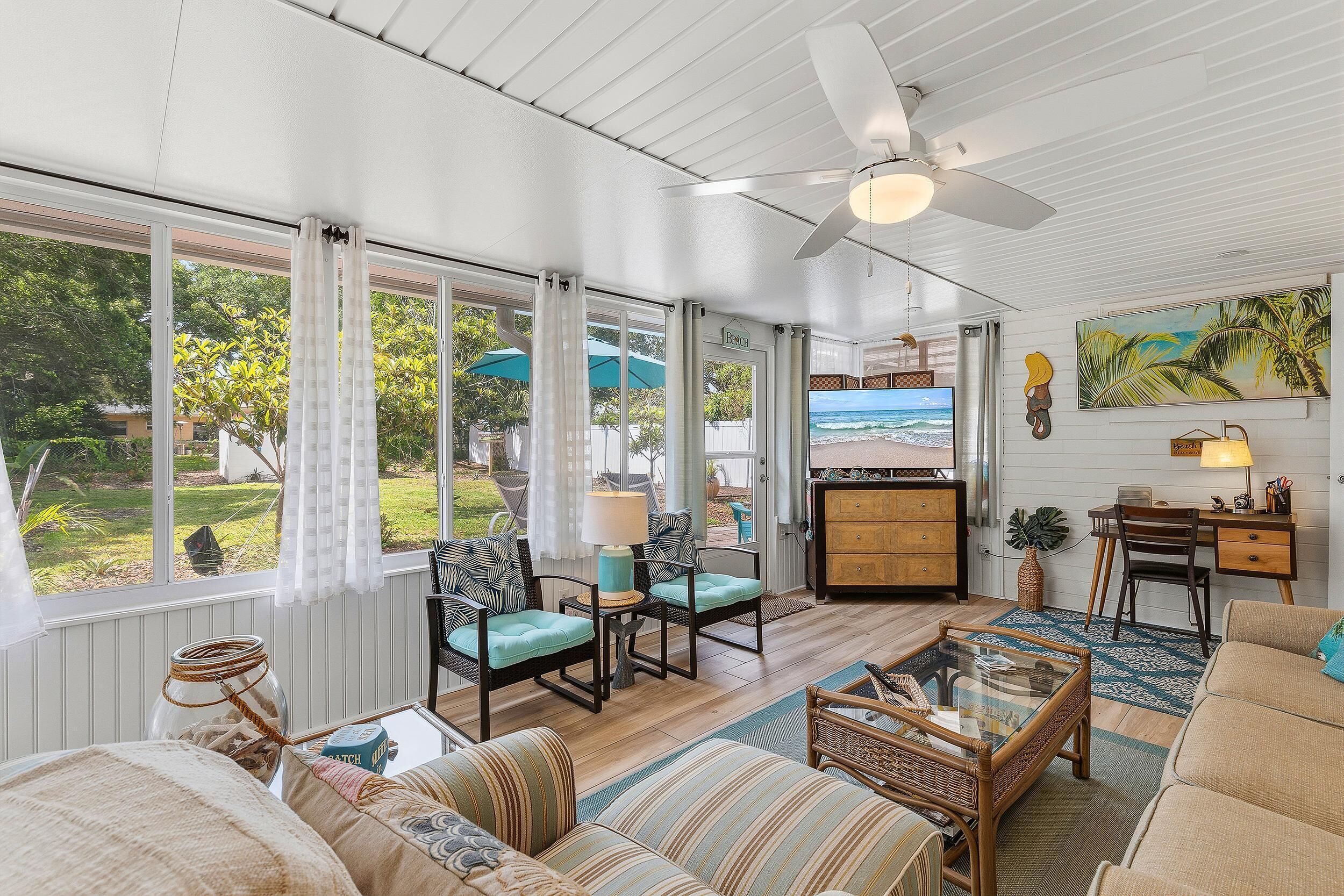 A spacious living room with a large window, a ceiling fan, and a television.