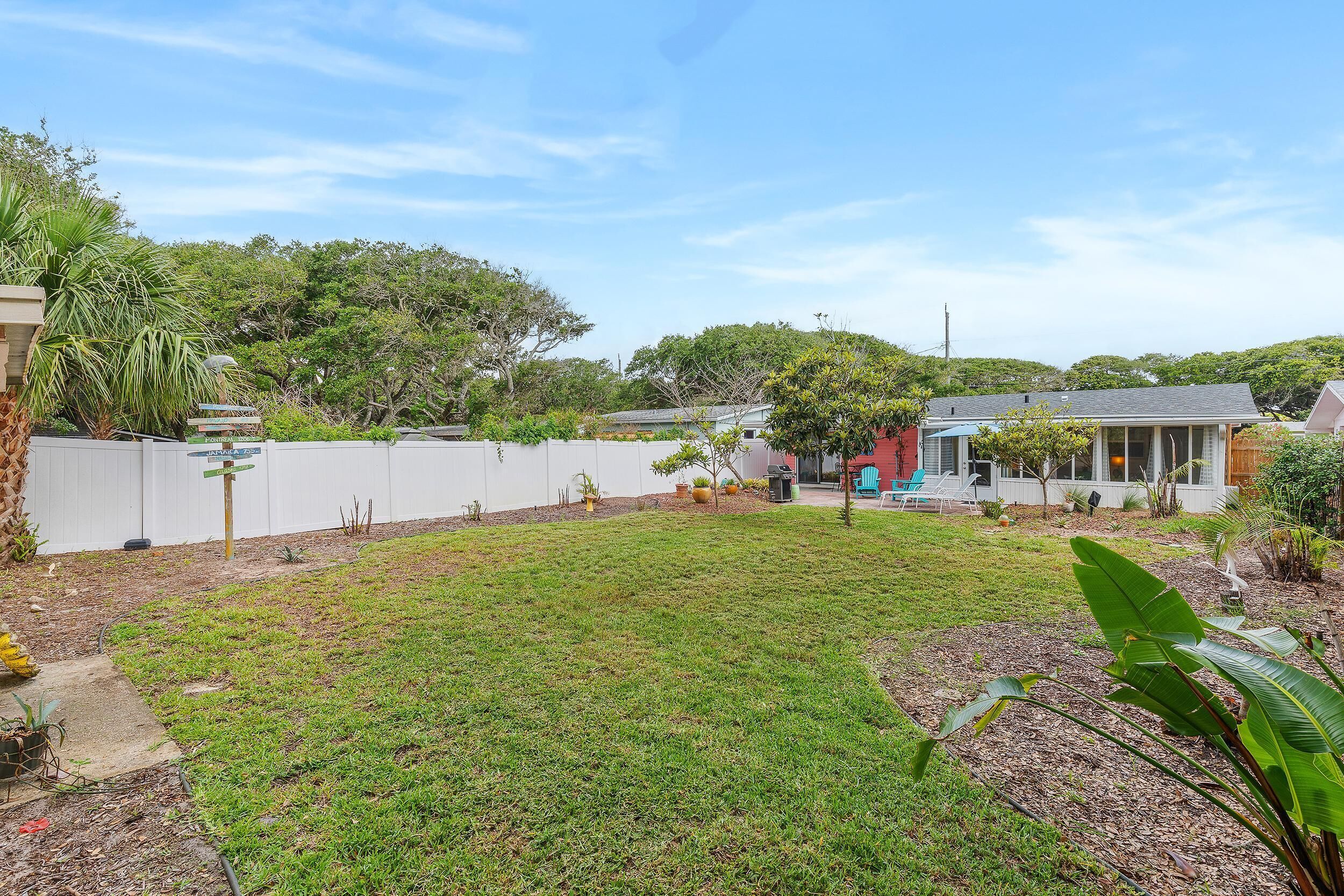 Un patio trasero residencial con césped, una cerca blanca y una casa con tejado rojo.