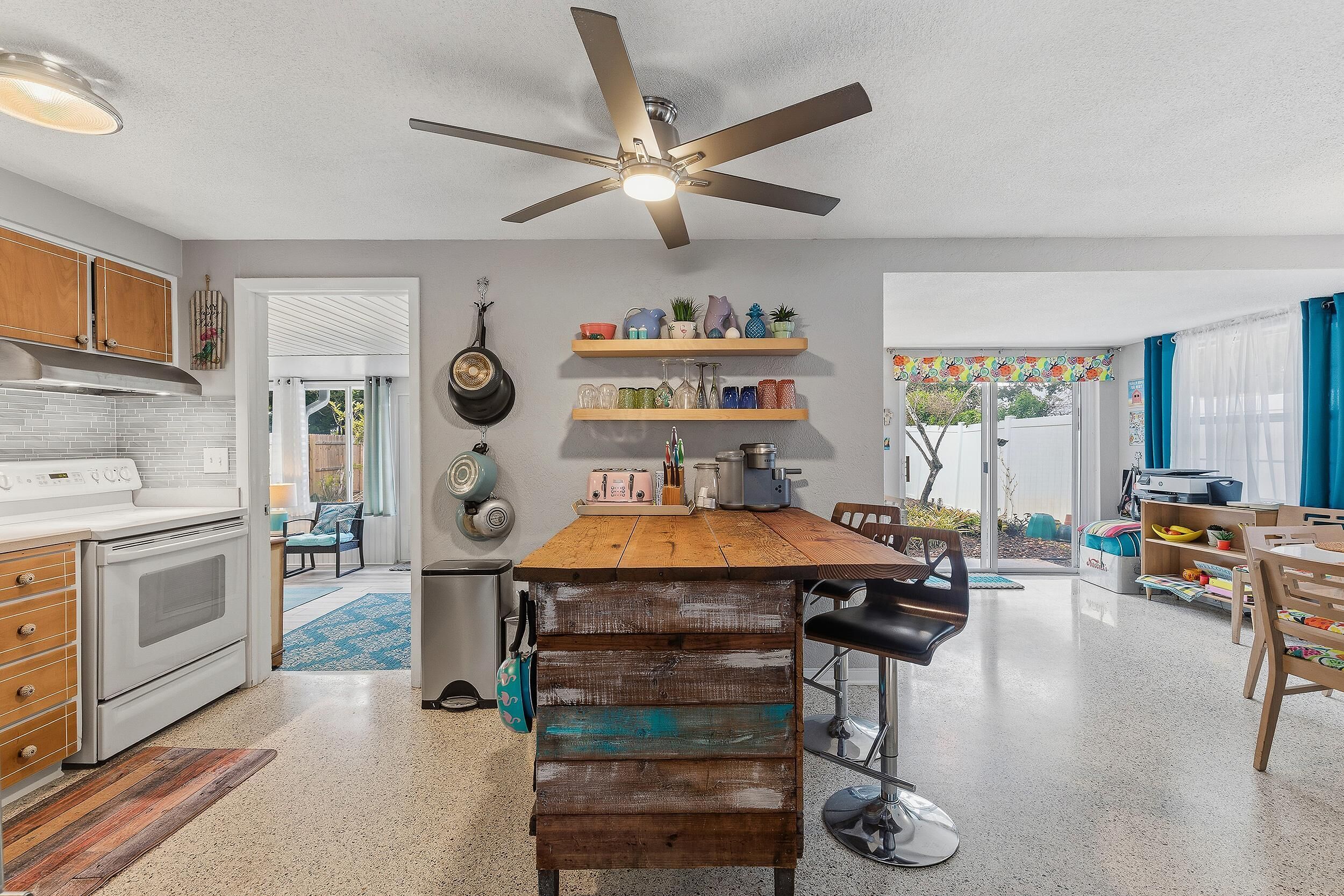 A kitchen with a central island, wooden cabinets, a ceiling fan, and a dining area with chairs and a table.