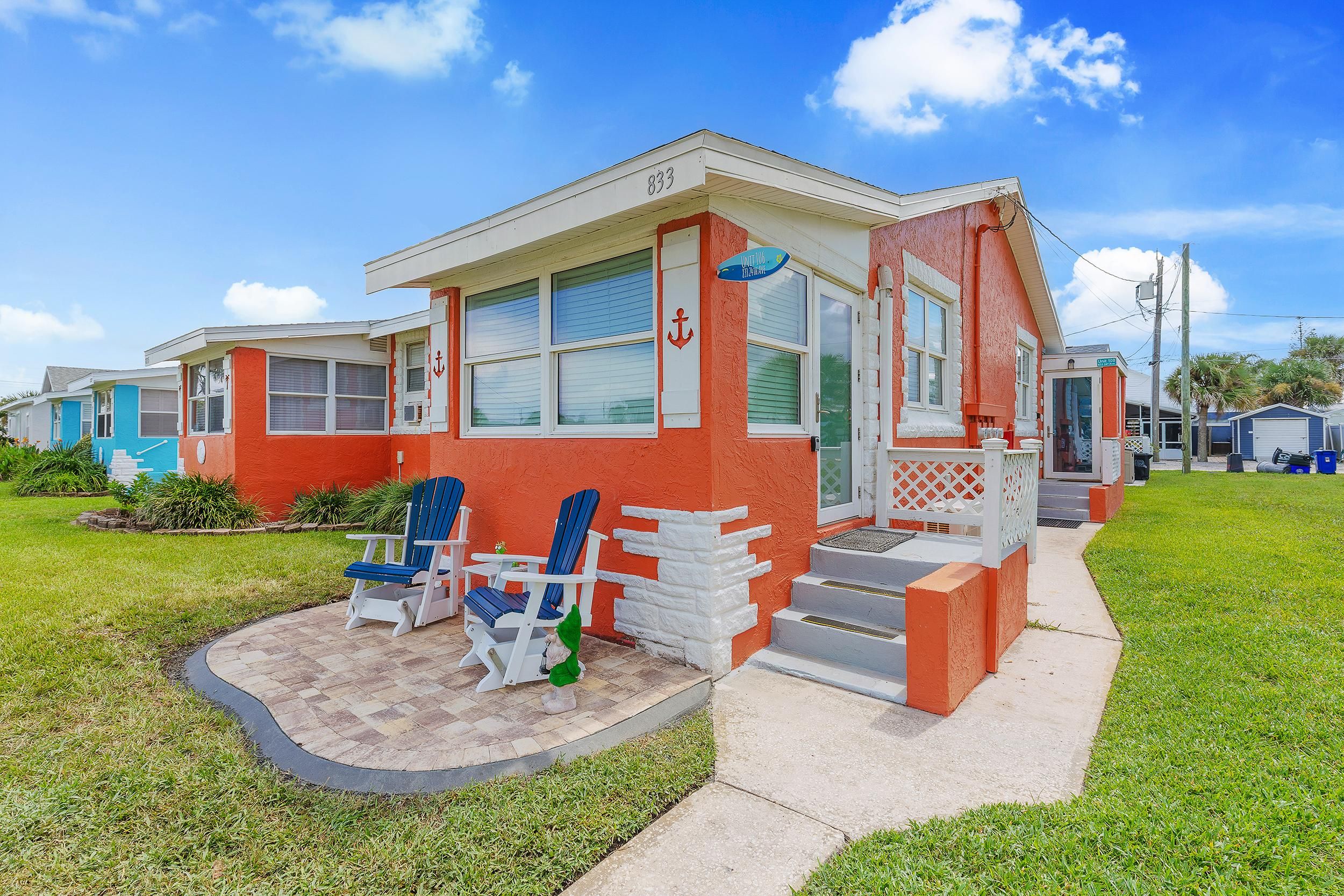A single-story building with a red exterior and white trim, featuring a small porch with two blue Adirondack chairs and a small table.