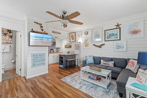 Ein wohnzimmer im Strandhausstil mit Fernseher, Sofa, Couchtisch und Kunstwerken.