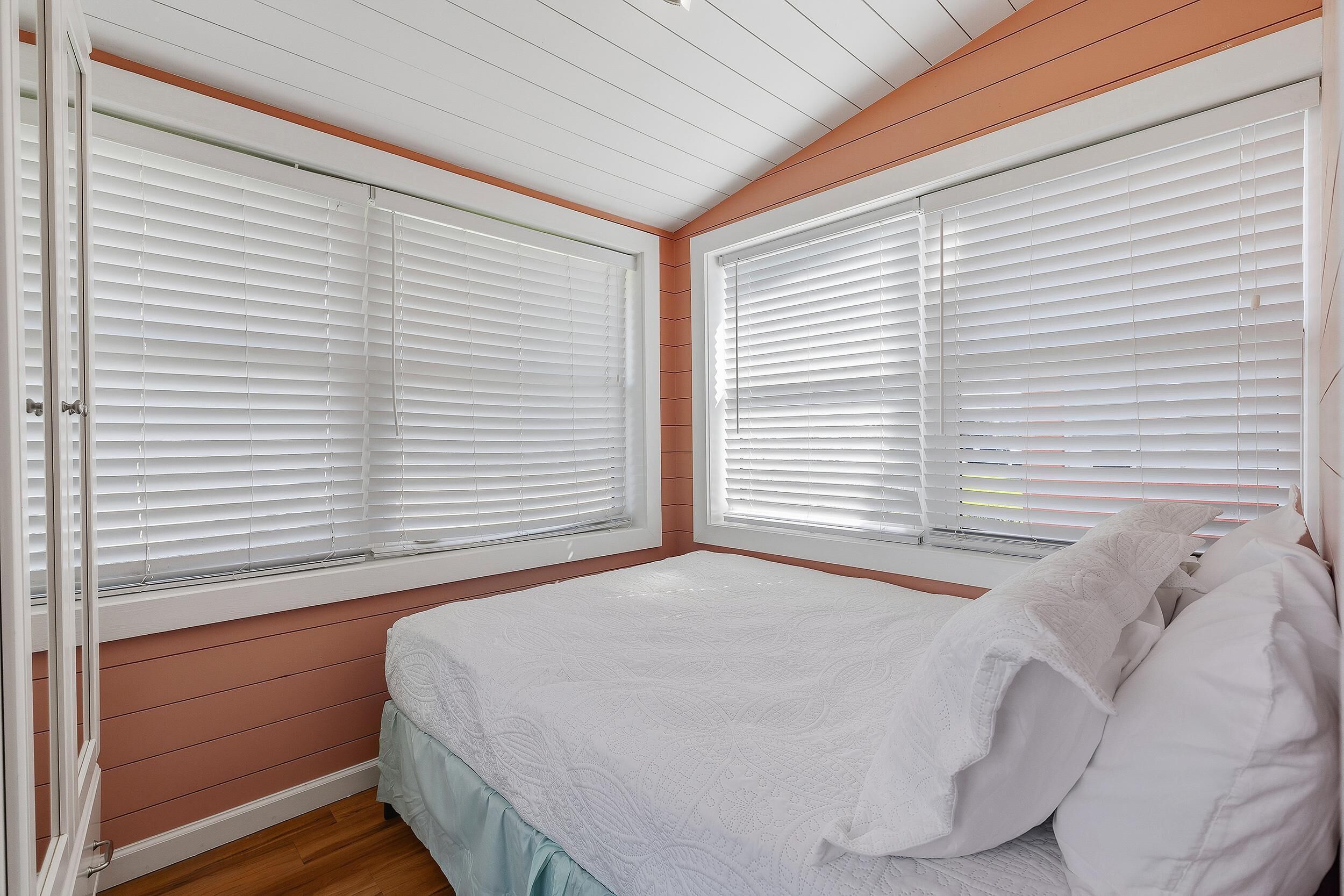 Ein Schlafzimmer mit einem Bett, weißen Jalousien und Holzvertäfelung.