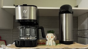 A kitchen with a coffee maker, a thermos, and a ceramic mug on the counter.