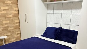 A bedroom with a bed, white wardrobe, and a small table.