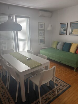 Ein Zimmer mit Esstisch, Stühlen, einem grünen Sofa und einem kleinen runden Tisch.