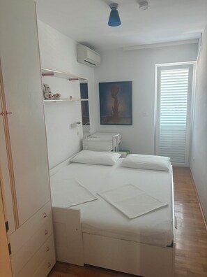 Ein Schlafzimmer mit Bett, Schrank, Nachttisch, Wand-Klimaanlage und Fenster mit Jalousien.