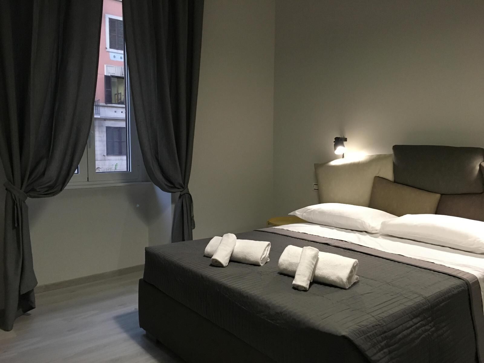 Une chambre d’hôtel avec un lit, des rideaux, une table de chevet et une lampe fixée au mur.