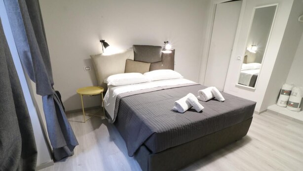 A modern bedroom with a large bed, bedside tables, a mirror, and a wardrobe.