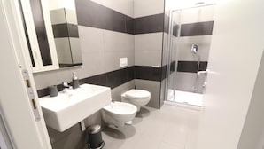 A modern bathroom with a white sink, two toilets, a shower, and a mirror.