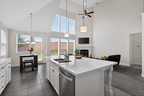 Een moderne keuken met een groot eiland, ingebouwde apparaten en een eethoek met een zwarte stoel.