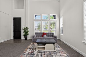 Una sala de estar con un sofá gris, una mesa de centro, una planta en maceta y una ventana con persianas.