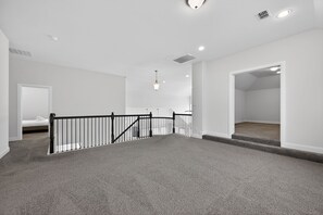 Een ruime, goed verlichte kamer met een hoog plafond, een zwarte balustrade en een vloerbedekking.
