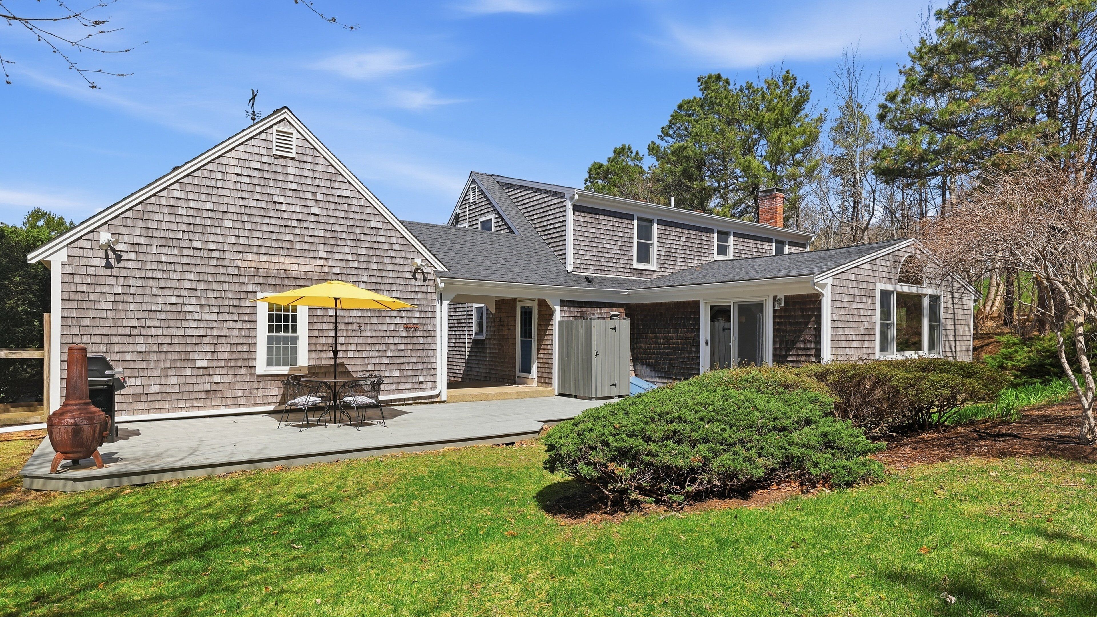 A two-story house with a covered patio, a grill, and a well-maintained lawn.