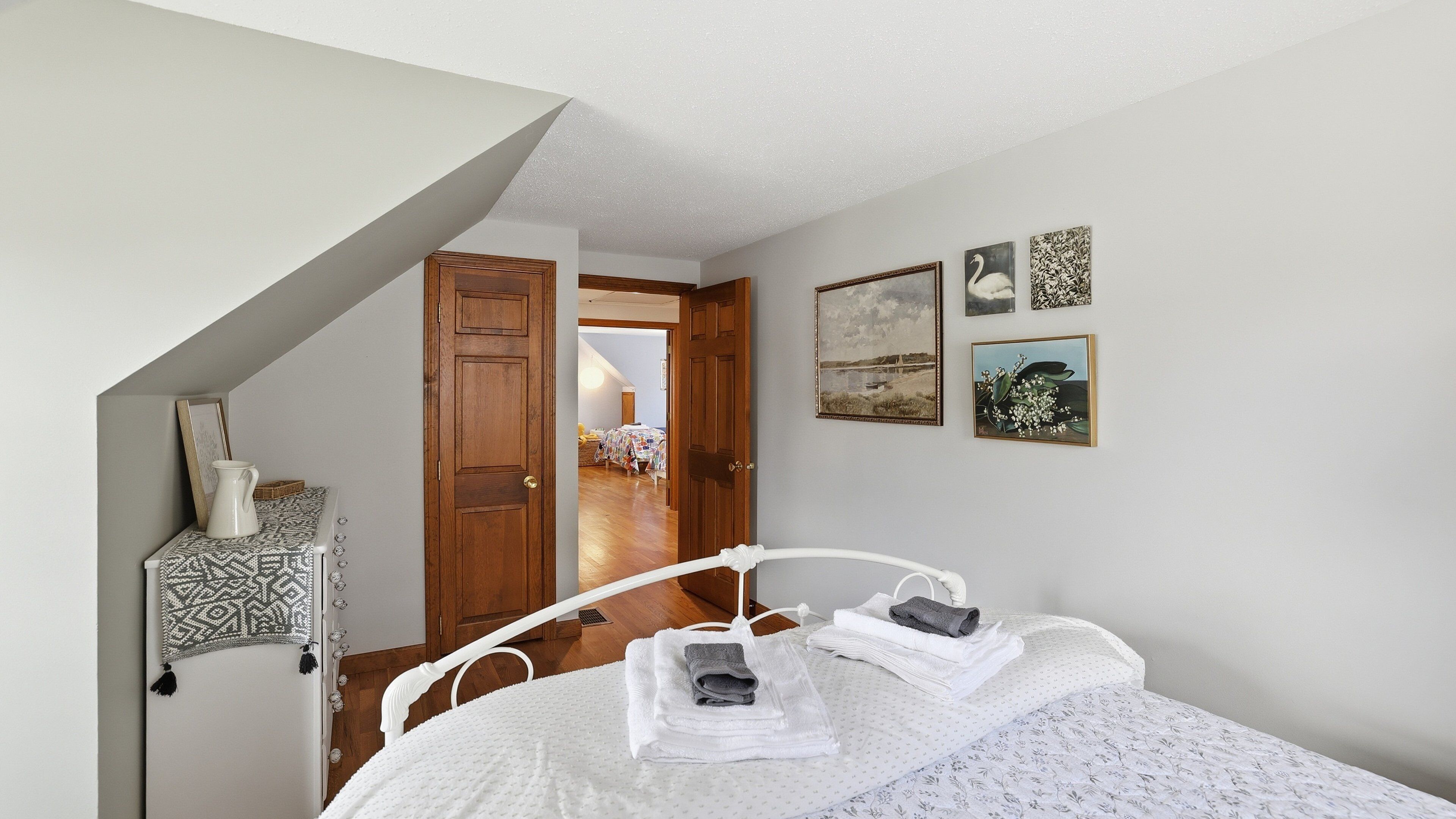 Un dormitorio con cama, cabecera blanca, puerta de madera y pared adornada con cuadros.