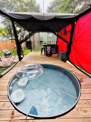 Ett bubbelbad med ett genomskinligt lock, ett trädäck och en röd tältkonstruktion.