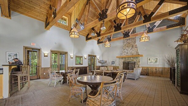 A spacious dining area with high ceilings, wooden beams, and a stone fireplace. - Collins Lake Mountain Condo #24| Pool, Sauna & Spa (Government Camp)
