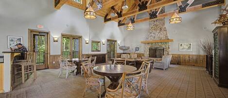 A spacious dining area with high ceilings, wooden beams, and a stone fireplace.
