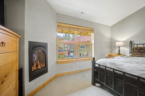 Ein Schlafzimmer mit Kamin, Bett, Nachttisch und Fenster mit Blick auf Gebäude.