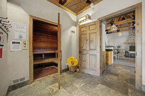Ein rustikales Interieur mit Sauna, Holzbänken, Steinplattenboden und Kamin aus Stein.