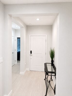 Un pasillo con una puerta blanca, una planta en maceta y una mesa con marco negro.
