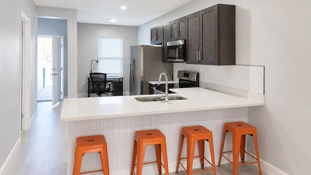 Una cocina moderna con una isla central, armarios oscuros y taburetes naranjas.