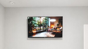 Una habitación con un televisor montado en la pared, un mueble de entretenimiento negro debajo y dos cestas de mimbre.