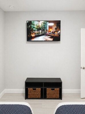 Una habitación con un televisor montado en la pared, un mueble de entretenimiento negro debajo y dos cestas de mimbre.