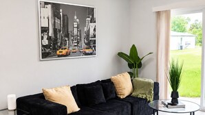 Una sala moderna con un sofá seccional negro, una mesa de centro de vidrio y una pintura de un paisaje urbano en la pared.