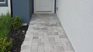 Una entrada de casa moderna con una puerta blanca, un camino de ladrillo gris y una pared exterior azul.