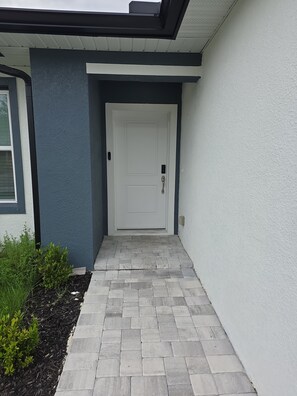 Una entrada de casa moderna con una puerta blanca, un camino de ladrillo gris y una pared exterior azul.