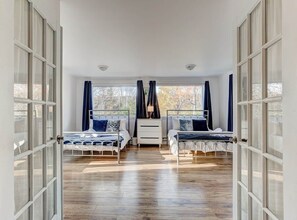 Ein Schlafzimmer mit zwei Betten, einer weißen Kommode und einem Fenster mit Vorhängen.