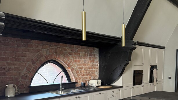 Een moderne keuken met een bakstenen muur, witte kasten, een groot eiland en hanglampen.