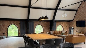 Een ruime eethoek met een hoge plafond, open bakstenen muren en grote ramen.