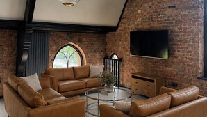 Een ruime loft met blootgelegde bakstenen muren, leren banken, een glazen salontafel en een flatscreen televisie aan de wand.