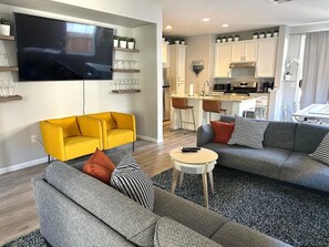 Ein modernes Wohnzimmer mit Flachbildfernseher, zwei Sofas, einem Couchtisch und einer Küche im Hintergrund.