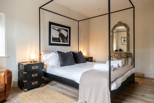 A bedroom with a four-poster bed, a large mirror, a framed picture on the wall, and a dresser with drawers.
