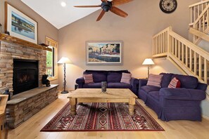 Ein Wohnzimmer mit Kamin, Deckenventilator, Treppe und einem großen Gemälde an der Wand.