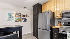A compact kitchen with a refrigerator, microwave, and oven. There are wooden cabinets and a small dining table. - "Chalet" lake house/walking path/fenced yard/dock (Winter Haven)