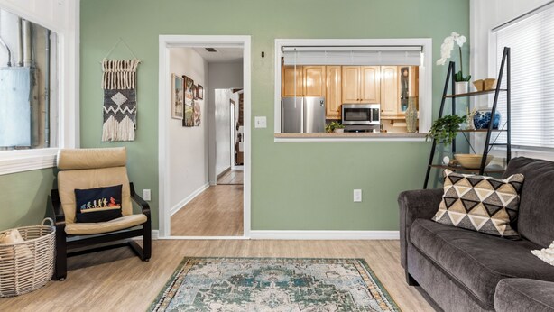 A living room with a sofa, a chair, a rug, and a kitchen visible through an open doorway.