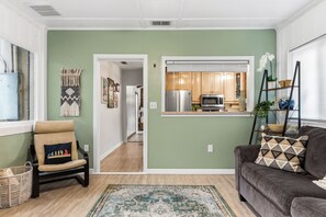 A living room with a sofa, a chair, a rug, and a kitchen visible through an open doorway.