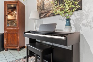 A piano with a laptop on top, a wooden cabinet, a lamp, and a plant.