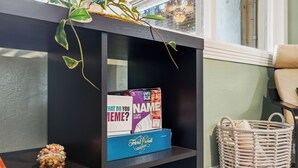 A shelf with a plant, a game box titled 'What Do You Meme?', and a woven basket. - "Chalet" lake house/walking path/fenced yard/dock (Winter Haven)